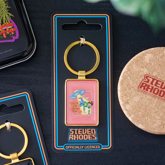 A vintage enamel keyring by Steven Rhodes, featuring a cartoon of a person beneath blue mushrooms on pink with the phrase “Get Off My Shrooms.” Supplied with a gold-coloured ring and branded packaging—perfect as a Steven Rhodes gift.