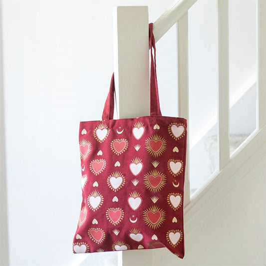 A stylish tote bag featuring pink, white, and gold heart patterns hangs from a white stair banister. This reusable Valentine’s Day gift bag brings charm to the clean, minimal decor.