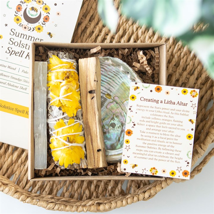 A Litha Festival spell kit sits in a woven basket, featuring a yellow flower-wrapped smudge stick, abalone shell, wooden sticks, and an instruction card titled Creating a Litha Altar with sunflower illustrations.