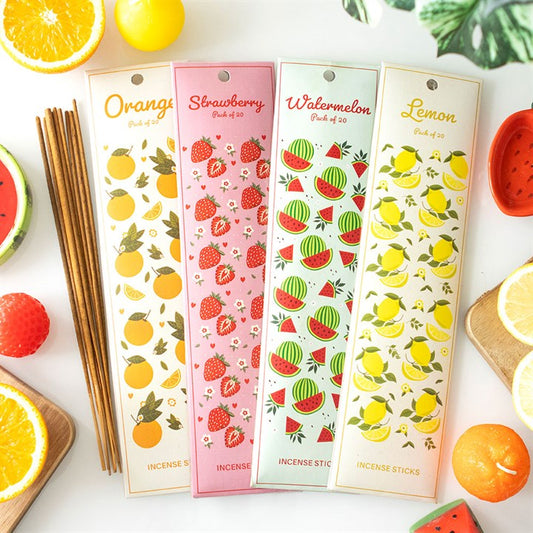 Four colourful Tutti Frutti incense stick packs are displayed on a white surface, each featuring fruit illustrations—orange, strawberry, watermelon, and lemon. Fresh fruit slices and sweet scents surround the incense packs.