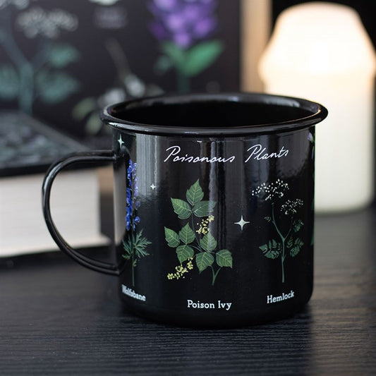 A gothic mug labelled Poisonous Plants, featuring illustrations of nightshade, poison ivy, and hemlock, sits on a dark surface with a book and a softly glowing candle in the blurred background.
