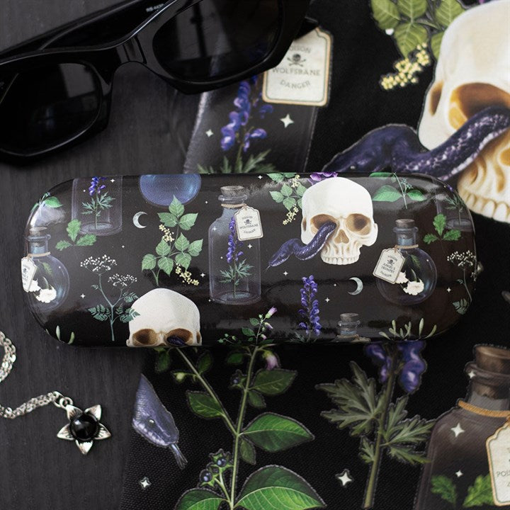 A glasses case with a dark, botanical design inspired by gothic aesthetics, featuring skulls, potion bottles, green leaves and purple flowers. Sunglasses and a matching cleaning cloth complete the striking look.