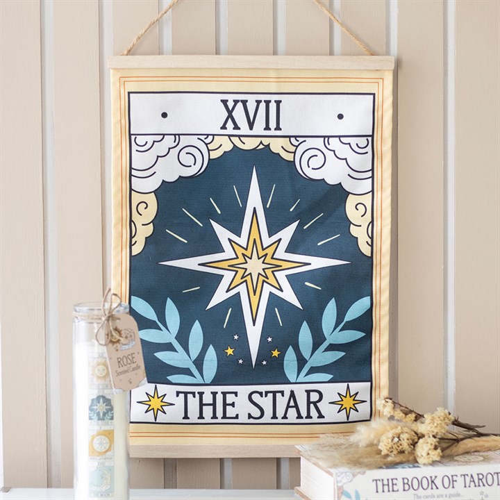 A fabric wall hanging of The Star tarot card, featuring a radiant celestial design with stars, clouds, and laurel leaves. Labelled XVII at the top and THE STAR at the bottom, it also displays a jar and a book nearby.