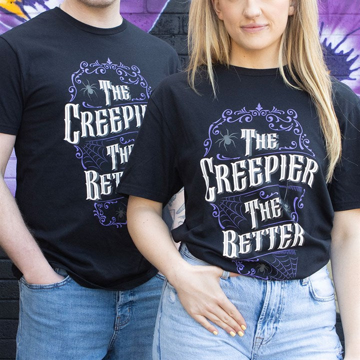 Two people stand side by side against a colourful graffiti wall, each wearing a spooky shirt with ornate white and purple lettering reading “The Creepier The Better,” decorated with spiders and cobwebs.
