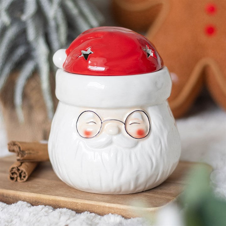 A ceramic oil burner in the shape of Father Christmas, complete with a red hat and spectacles, sits on a tray beside a cinnamon stick—perfect for diffusing festive essential oils and filling your home with Christmas spirit.