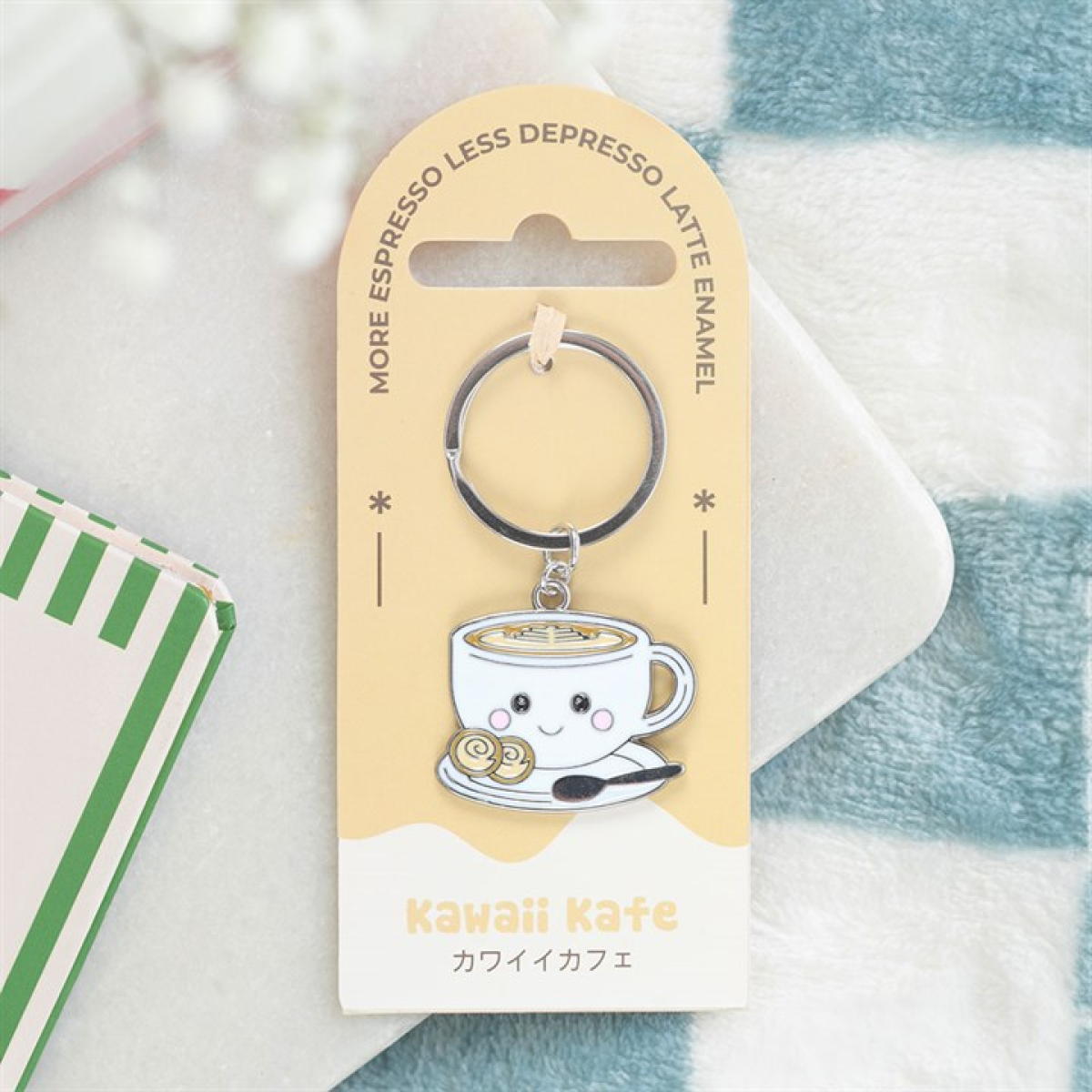 A charming enamel keyring featuring a latte cup and pastry is fastened to yellow packaging marked “Kawaii Kafe” in both English and Japanese. At the top, it says “MORE ESPRESSO LESS DEPRESSO LATTE ENAMEL.”.