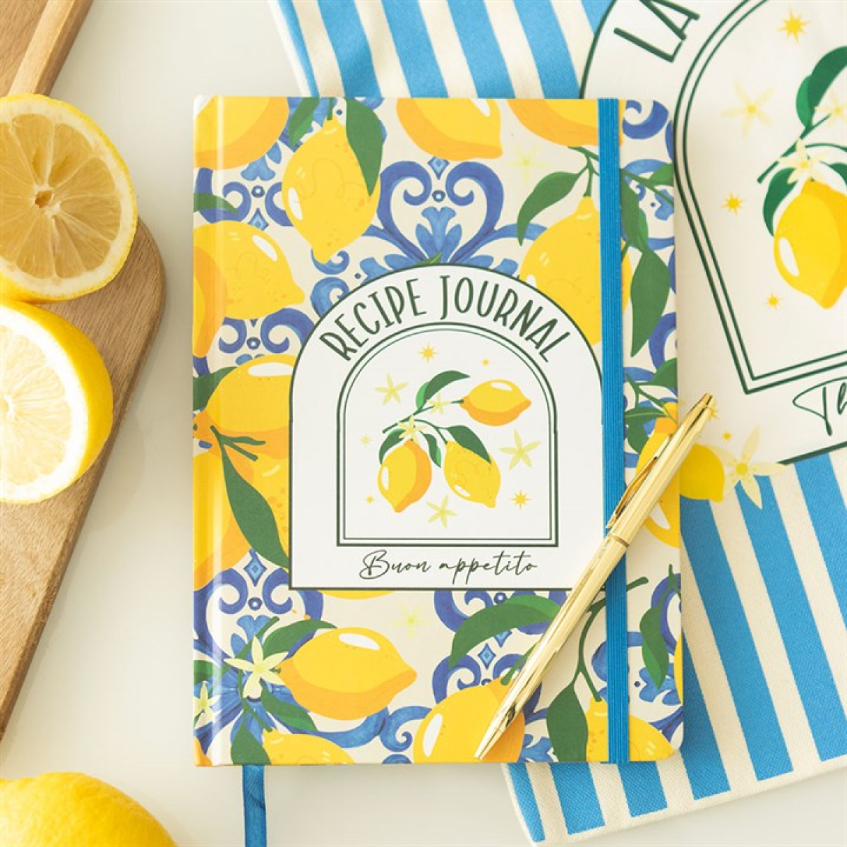 A colourful A5 recipe journal with a lemon-themed cover, gold pen, and “Bon appétit” rests on a blue-striped cloth beside sliced lemons on a chopping board—ideal for sparking Italian cooking inspiration.
