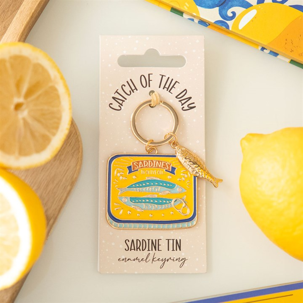 A quirky enamel keyring with a yellow sardine tin motif and gold fish charm, offered as an ideal Italian gift. The Catch of the Day packaging is adorned with sliced lemons.