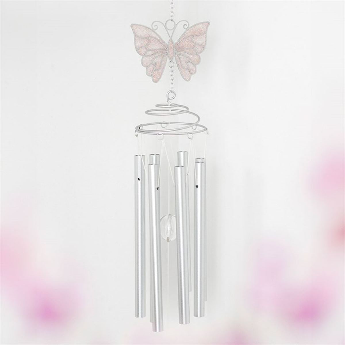 A delicate butterfly windchime displays five silver tubes, a spiral top, and a central crystal pendant suspended beneath a pink butterfly ornament. The white background is softly tinged with pink in the corners.