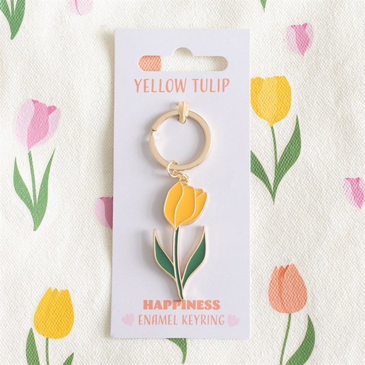 A golden-yellow tulip keyring with a delightful enamel charm is affixed to a card reading YELLOW TULIP and HAPPINESS ENAMEL KEYRING, making an adorable gift. The background features a vibrant floral tulip pattern.