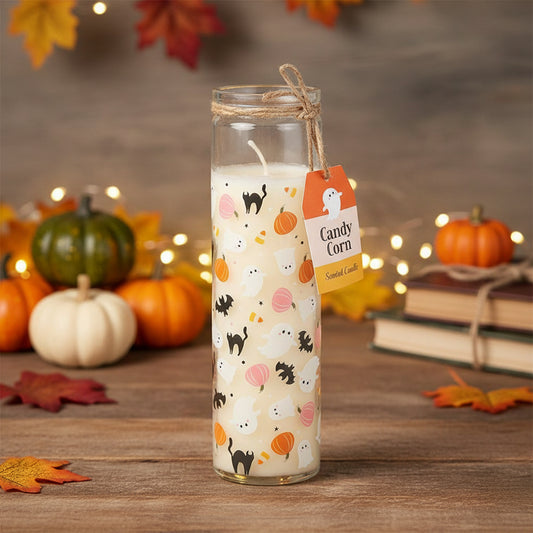 A tall Halloween candle adorned with ghosts, bats, pumpkins, and candy corn rests on a wooden table. A “Candy Corn” tag is tied with twine among mini pumpkins, books, leaves, and fairy lights for a cosy autumn atmosphere.