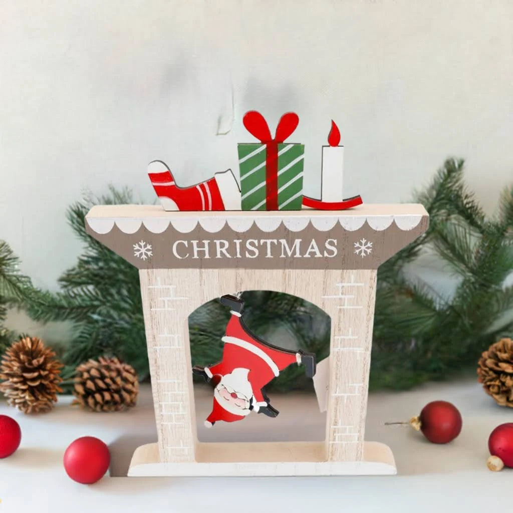 A festive, fireplace-themed Christmas decoration displays Father Christmas upside down in a chimney labelled CHRISTMAS, with presents, a stocking, and a candle. Pinecones, fir branches and red baubles enhance the cheerful backdrop.