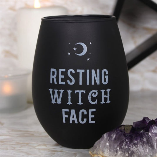 Part of our Black Magic collection: A matte, frosted black wine glass displays “Resting Witch Face” in white gothic lettering, featuring a crescent moon, stars, a lit candle, and purple crystals for a mystical effect.