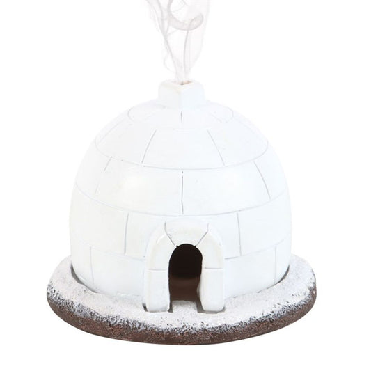 A small, white, dome-shaped igloo incense cone burner sits on a snowy base. Smoke rises from the top vent, adding charm to this unique winter décor with an arched entrance at the front.