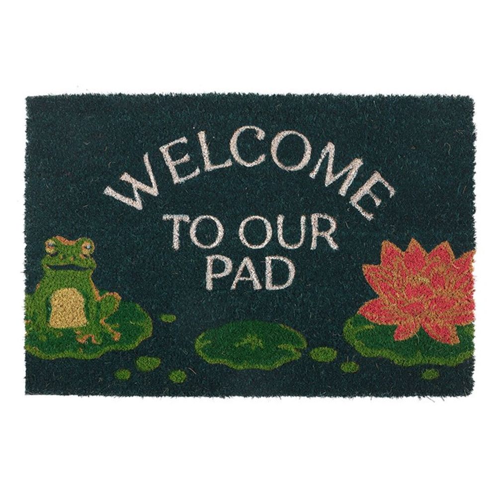 A welcome doormat with the text WELCOME TO OUR PAD features a charming frog design, complete with a cartoon frog on a lily pad to the left and a vibrant pink lotus flower to the right. Perfect for indoor use, its dark green background beautifully complements shades of green, pink, and white.