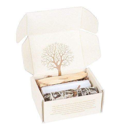 An open cream-coloured box with an illustration of a tree on the inside of the lid, containing bundles of sage, Palo Santo sticks, and a white candle, all neatly arranged on brown paper padding.