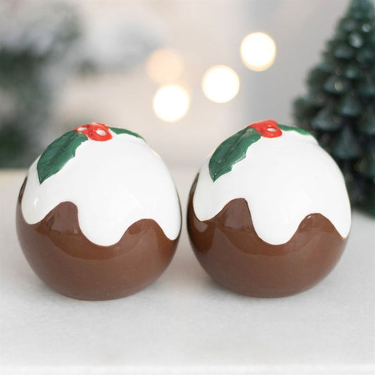 Two round ceramic Christmas pudding salt and pepper shakers, decorated with white icing, holly leaves, and red berries, rest on a white surface—a charming addition to brighten your festive table this Christmas.