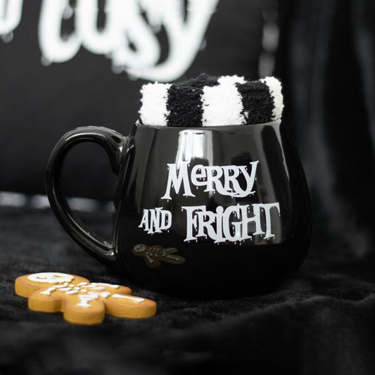 This cosy winter gift includes a spooky mug with "Merry and Fright" in white lettering, filled with a stripy sock. Two gingerbread biscuits complete this charming mug and sock gift set against a dark background.